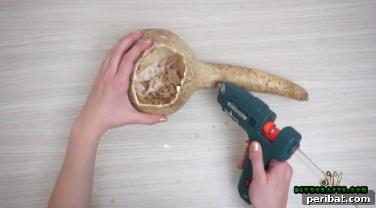 Minutes to Marvelous: 5 Easy Fall DIY Decor Projects 26 Adding decorative straw around the rim of the hollowed gourd using a hot glue gun, enhancing its natural, rustic appearance.