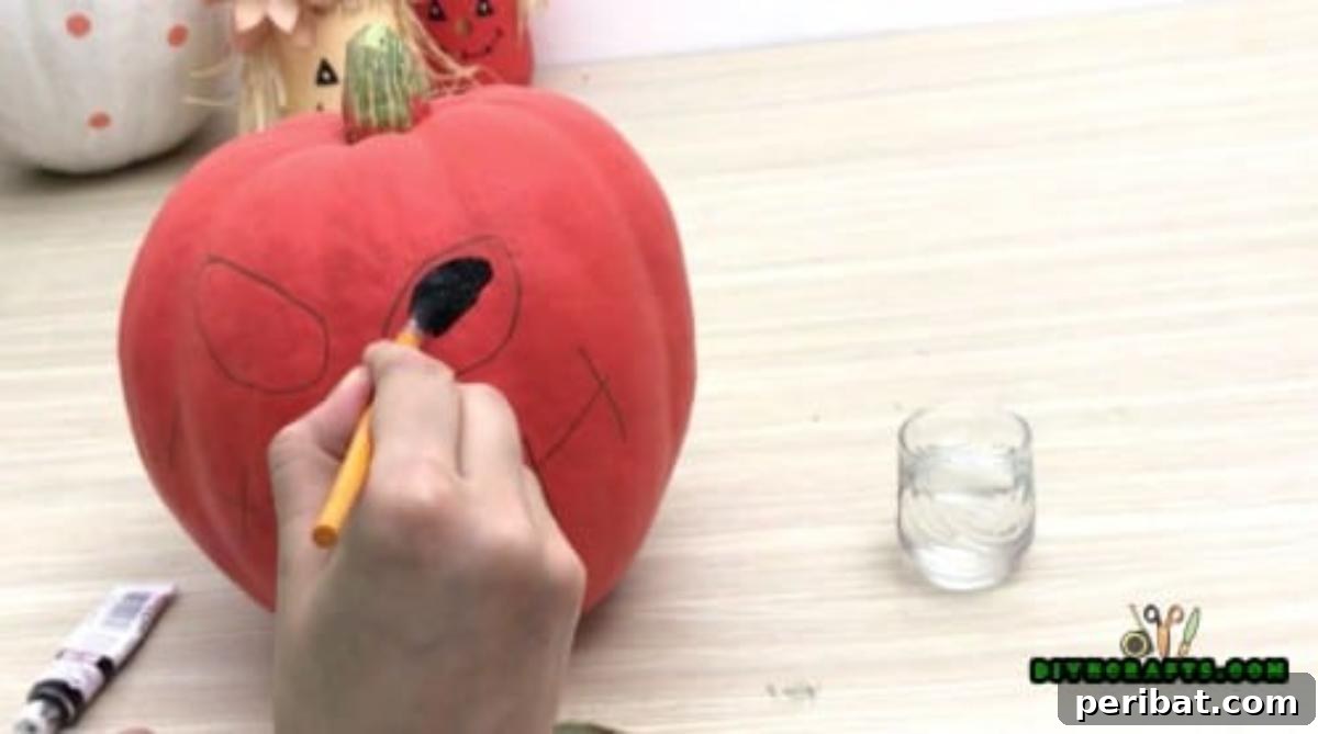 Step 3: Painting the sketched eye outlines black on the pumpkin, creating a strong contrast and spooky look.
