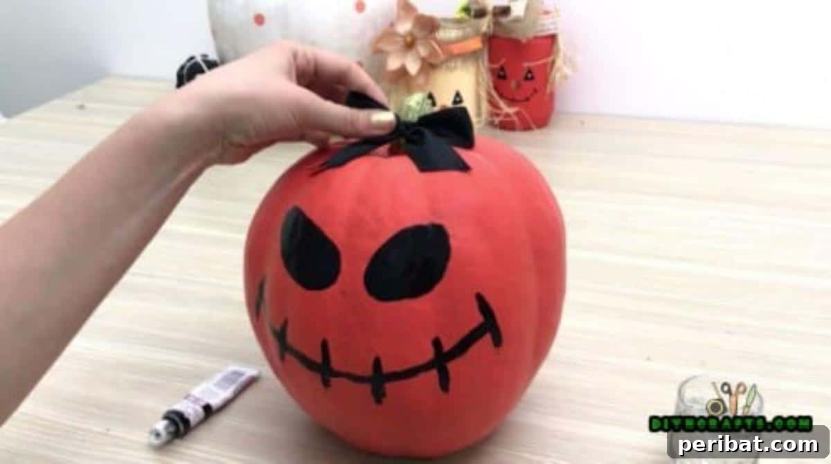 Step 5: Attaching a black bow to the pumpkin's stem, adding a decorative touch that emphasizes the painted features.
