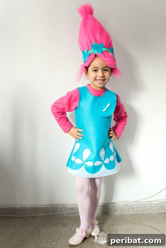 75 Effortless DIY Halloween Costumes That Kids Adore 14 A happy girl in a bright DIY Poppy the Troll costume standing by a white wall, ready for fun