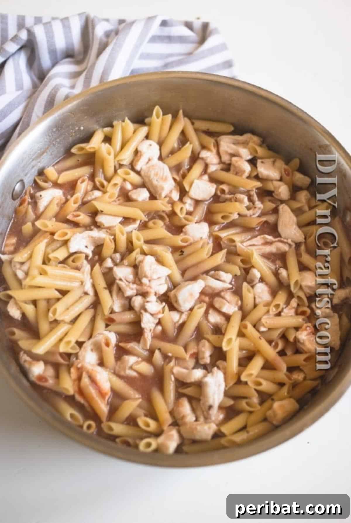 The Ultimate Easy Skillet Chicken Pasta 5 Uncooked pasta, tomato sauce, and seasonings being added to the browned chicken in a skillet, ready for simmering.