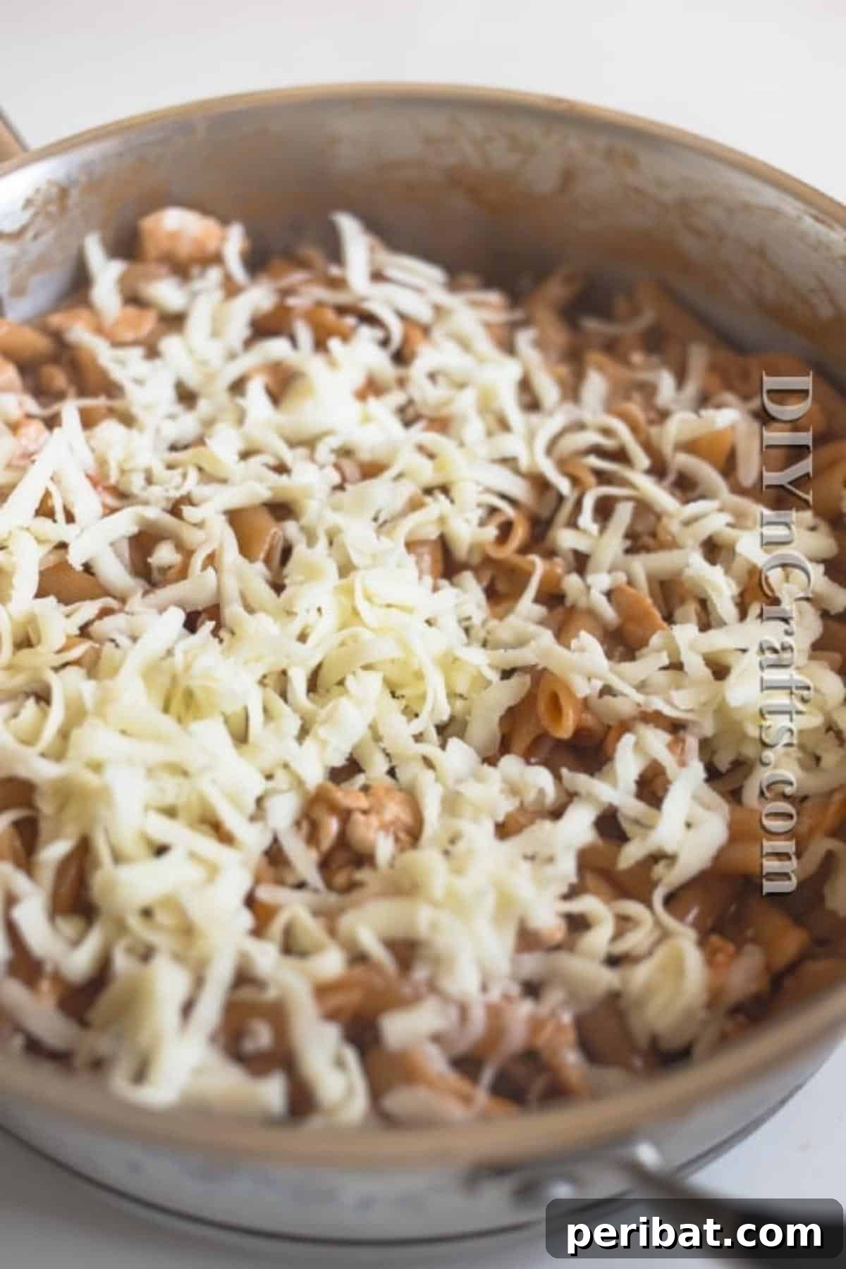 The Ultimate Easy Skillet Chicken Pasta 6 Shredded mozzarella cheese being sprinkled over the top of the chicken pasta skillet, ready to melt.