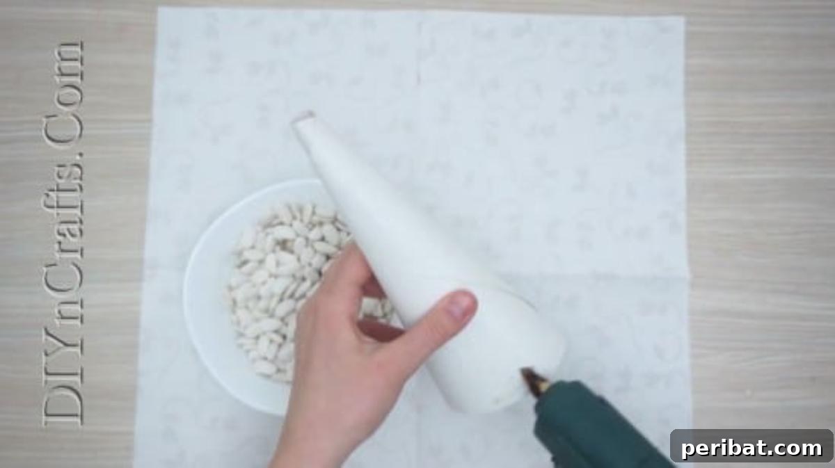 Hot gluing various beans onto a paper cone base for a textured Christmas tree.