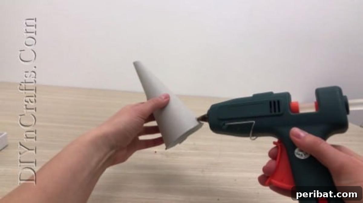 Hot gluing faux flower petals onto a paper cone, starting from the base.