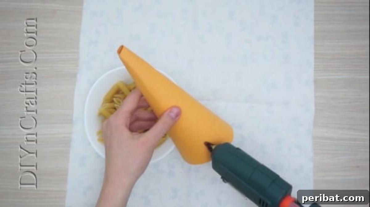 Hot gluing pasta pieces onto a paper cone, creating a textured surface.
