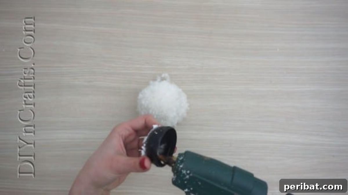 Snowman - Attaching a small hat to the pom-pom snowman's head with hot glue