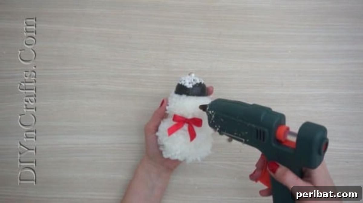 Snowman - Adding decorative elements like a bow and ball bearings for eyes to the pom-pom snowman