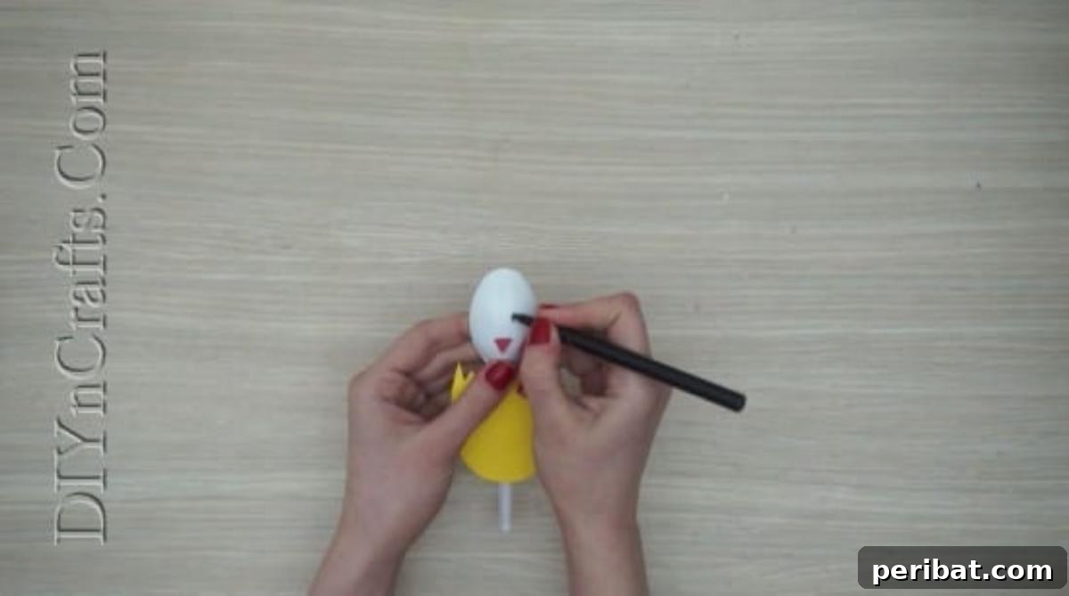 Spoonfuls of Fun 5 Easter Crafts for Kids Using Plastic Spoons 11 A black marker is being used to draw two small eyes onto the plastic spoon, completing the chick's face above its orange beak.
