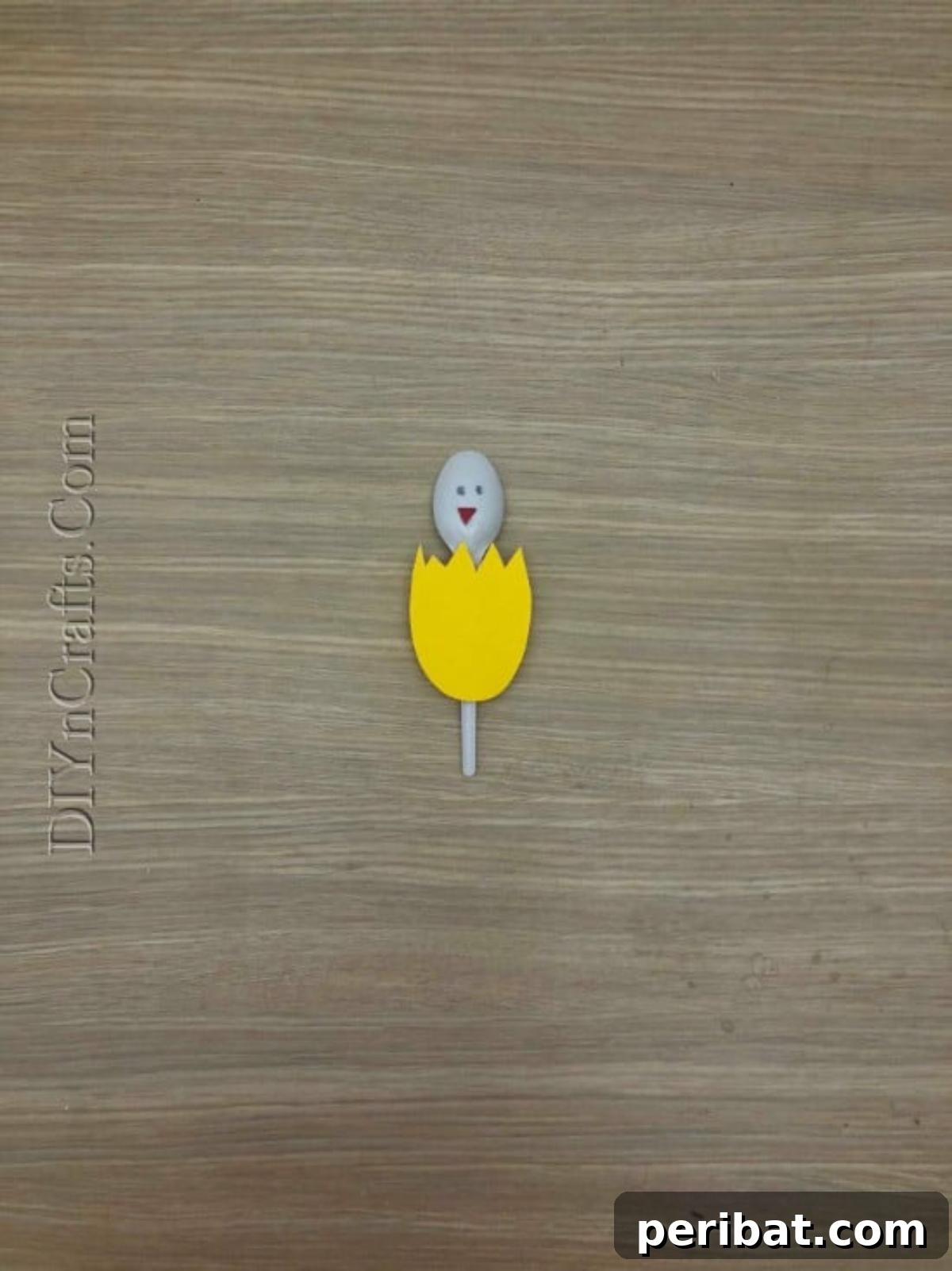 Spoonfuls of Fun 5 Easter Crafts for Kids Using Plastic Spoons 12 The finished Hatched Chick Spoon craft, showing a plastic spoon with a yellow cracked eggshell, an orange beak, and drawn eyes.