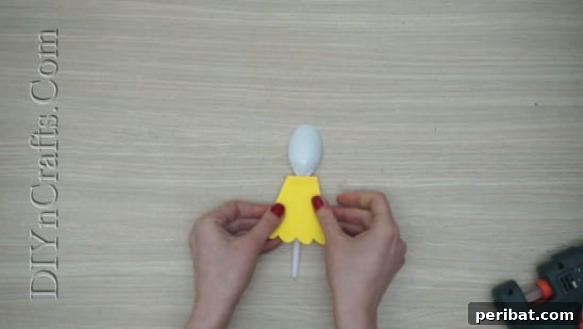 Spoonfuls of Fun 5 Easter Crafts for Kids Using Plastic Spoons 13 A piece of yellow construction paper is being cut into a rounded shape to form the chick's body for the spoon craft.