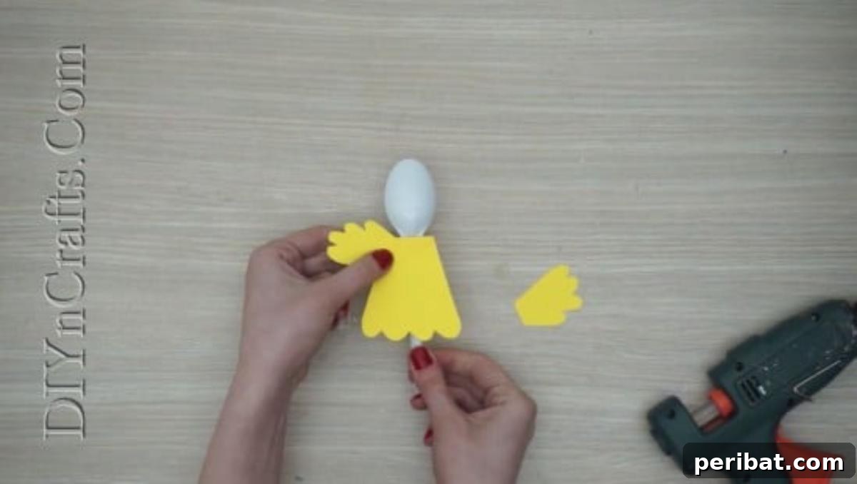 Spoonfuls of Fun 5 Easter Crafts for Kids Using Plastic Spoons 14 Two yellow paper wing shapes are being glued onto the sides of the yellow chick body, which is already attached to a plastic spoon.