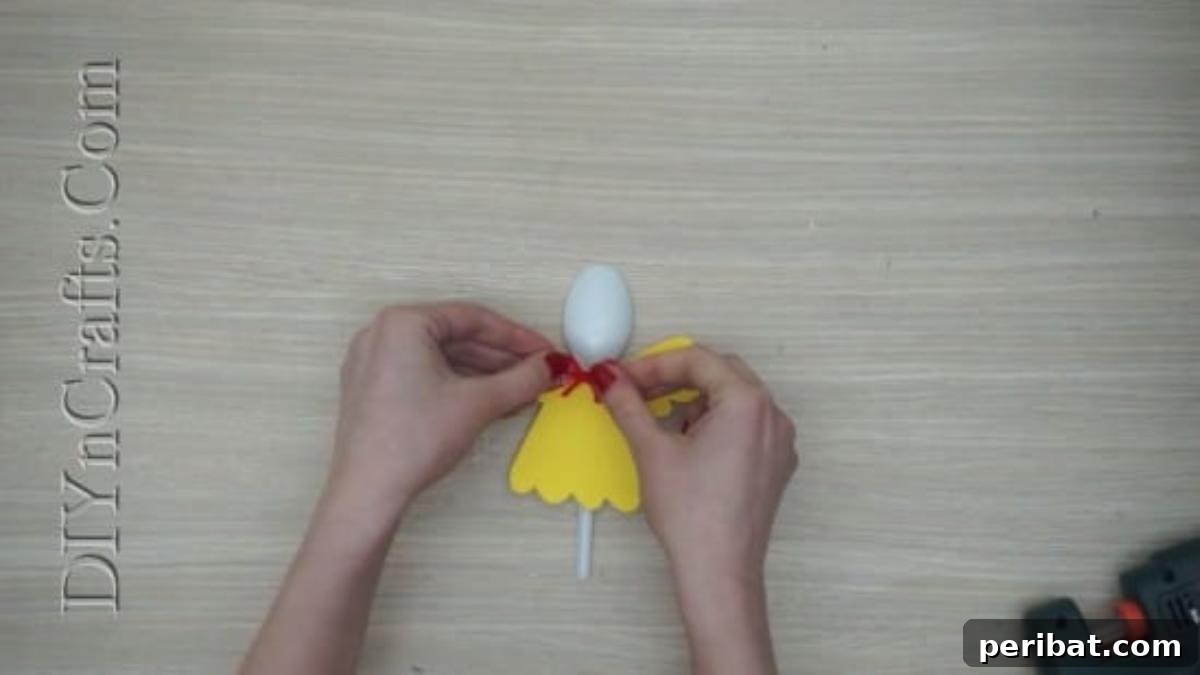 Spoonfuls of Fun 5 Easter Crafts for Kids Using Plastic Spoons 15 A small pink bow is being glued onto the neck area of the yellow chick spoon craft.