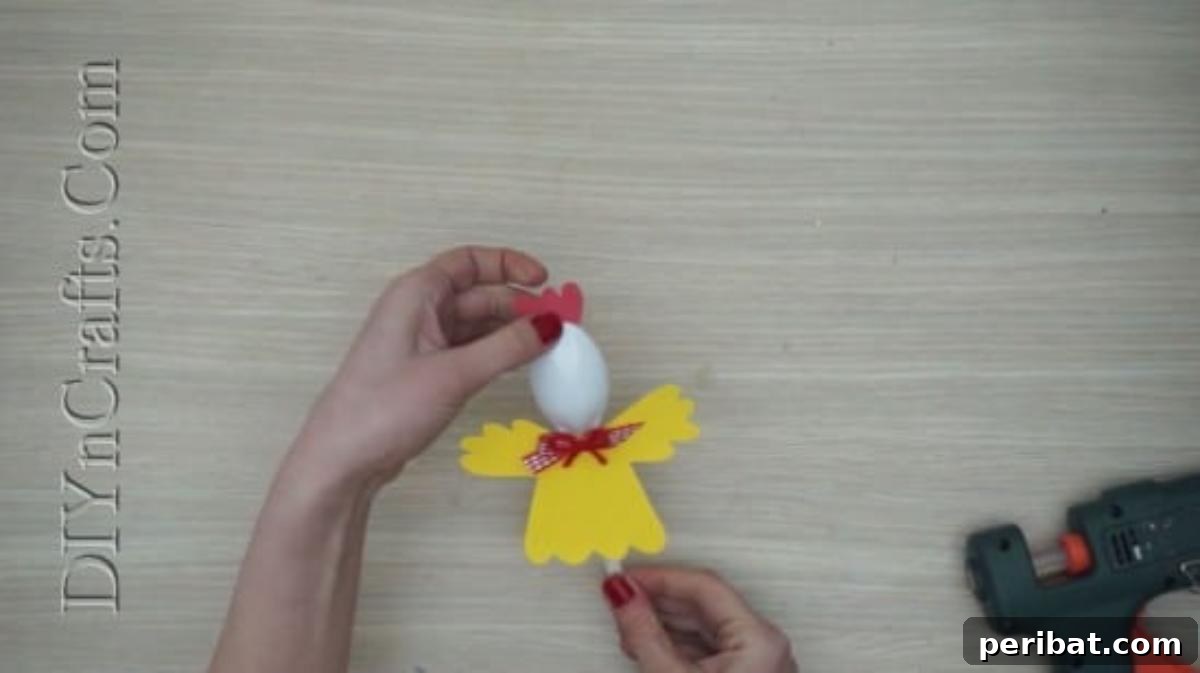 Spoonfuls of Fun 5 Easter Crafts for Kids Using Plastic Spoons 16 A red paper comb shape is being glued onto the top of the plastic spoon's head for the chick craft.