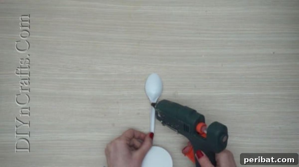 Spoonfuls of Fun 5 Easter Crafts for Kids Using Plastic Spoons 19 A white paper circle is being glued onto the thin handle part of a plastic spoon to form the bunny's body.