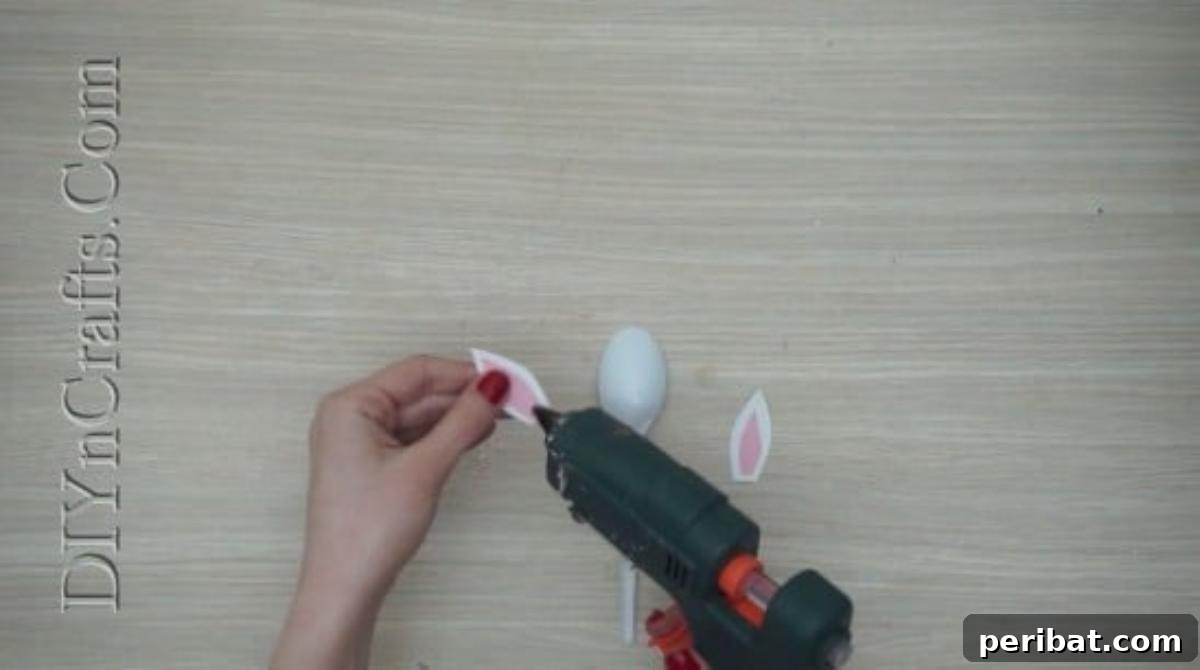 Spoonfuls of Fun 5 Easter Crafts for Kids Using Plastic Spoons 3 Two white and pink paper bunny ears are being held, ready to be glued onto a plastic spoon for an Easter craft.