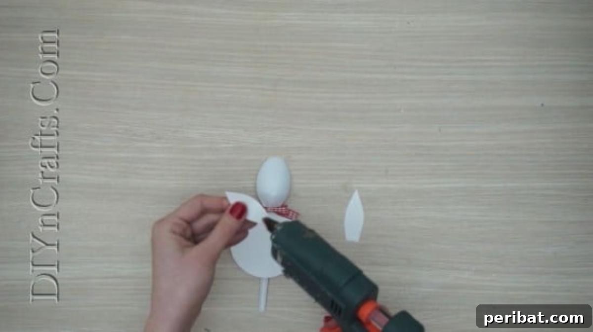 Spoonfuls of Fun 5 Easter Crafts for Kids Using Plastic Spoons 21 White paper bunny ears and a decorative bow are being glued onto the plastic spoon, which already has a white paper body.