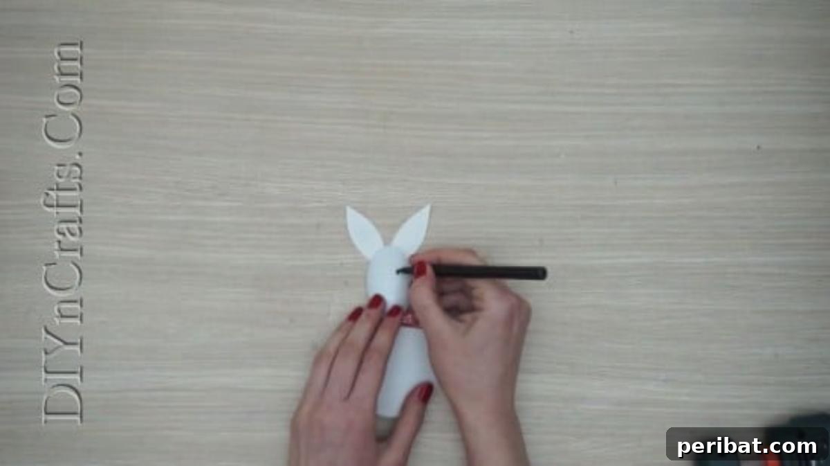 Spoonfuls of Fun 5 Easter Crafts for Kids Using Plastic Spoons 23 A black marker is being used to draw a friendly bunny face onto the plastic spoon, which is decorated with paper ears, a bow, and a round body.
