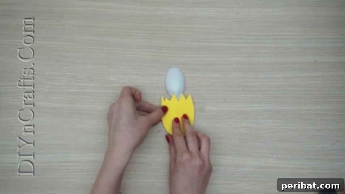 Spoonfuls of Fun 5 Easter Crafts for Kids Using Plastic Spoons 9 A yellow paper cutout resembling a cracked eggshell is being glued onto the convex side of a plastic spoon.