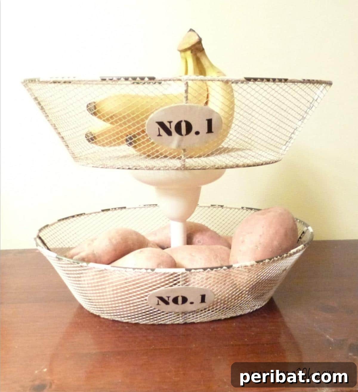A three-tiered hanging basket system, made from wire baskets and a central support, ideal for fruit storage.