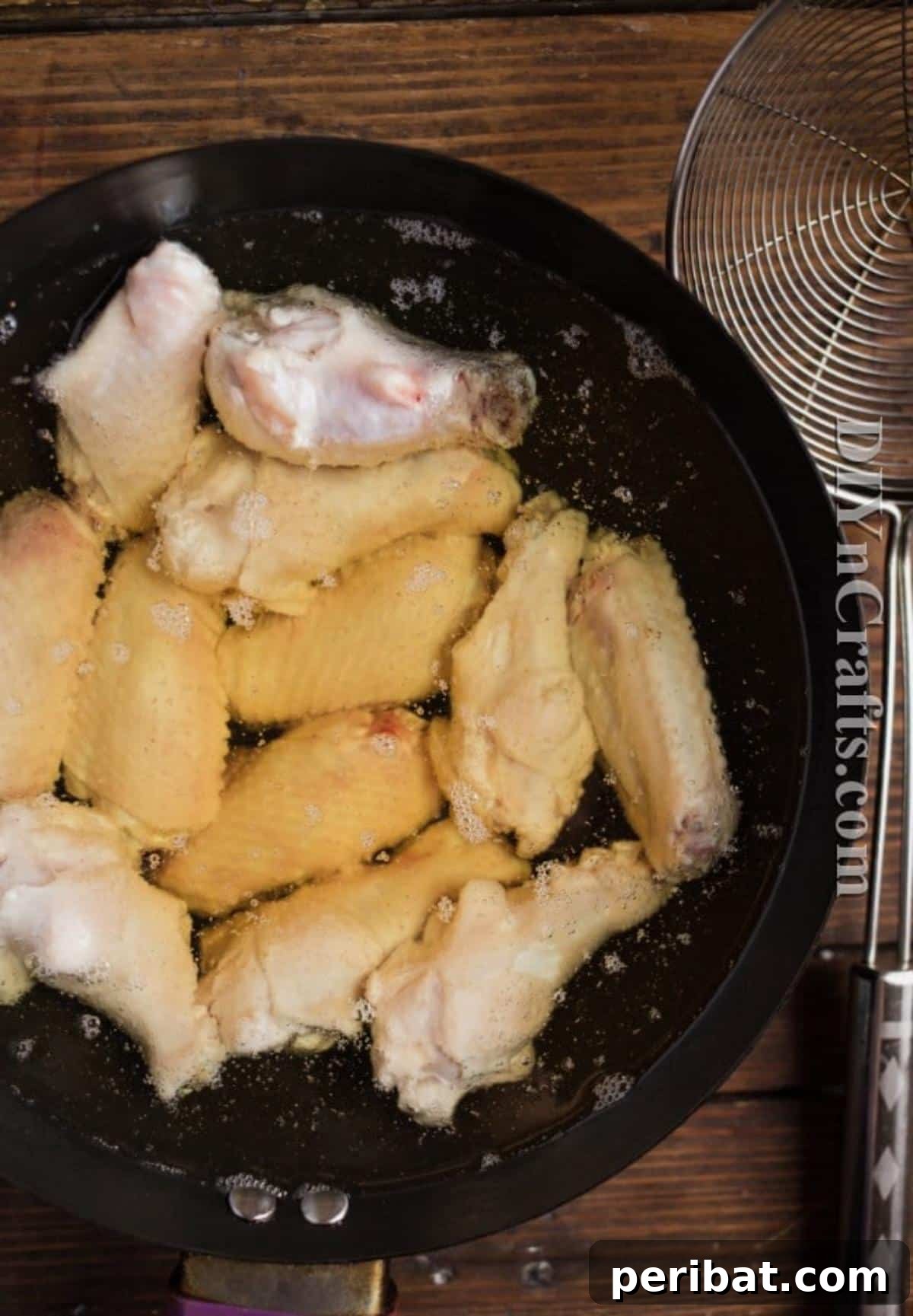 Raw chicken wings submerged in hot oil during the initial low-temperature frying stage, gently cooking.