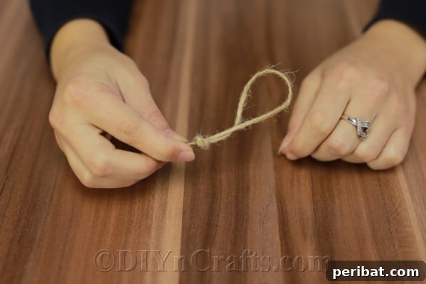 Forming a loop with natural twine, preparing it to be attached for hanging the ornament.