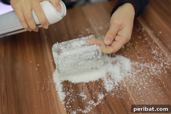 DIY Icy Glow Candle Jars 5 A glass jar being rolled in artificial snow to achieve an even, frosted coating, creating a wintry effect.