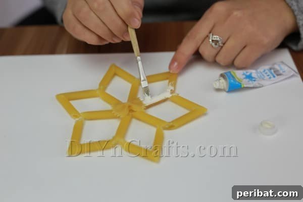 Dazzling Pasta Snowflake Christmas Ornaments 26 Applying white paint to a pasta snowflake with a brush for a traditional finish.
