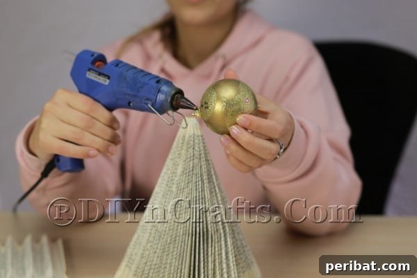 Upcycle an Old Book into a Stunning Christmas Angel 11 Hot gluing the Christmas ball ornament as the angel's head