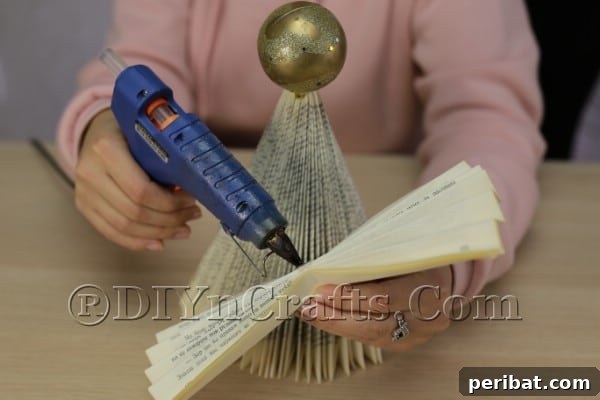 Upcycle an Old Book into a Stunning Christmas Angel 13 Hot gluing the fanned wings to the angel's back