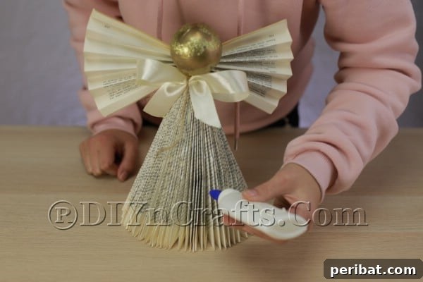 Upcycle an Old Book into a Stunning Christmas Angel 18 Applying glue to the edges of the angel's dress for glitter