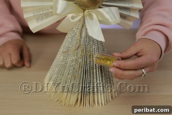 Upcycle an Old Book into a Stunning Christmas Angel 19 Sprinkling gold glitter onto the glued edges of the angel's dress