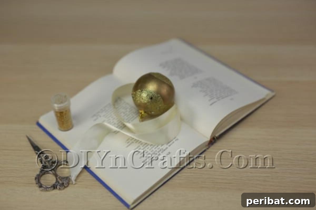 Upcycle an Old Book into a Stunning Christmas Angel 3 Essential materials and tools laid out for crafting a DIY book angel: an old book, ribbon, ornament, glue, and glitter.