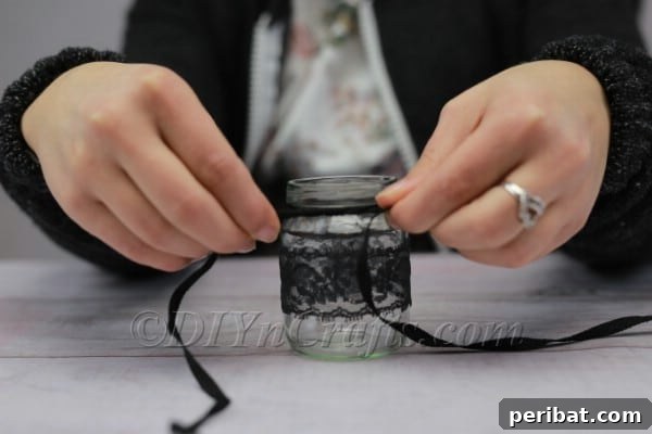 Craft a Charming Lace Lantern Effortlessly 7 Tying a decorative ribbon bow around the neck of the lace-adorned jar lantern