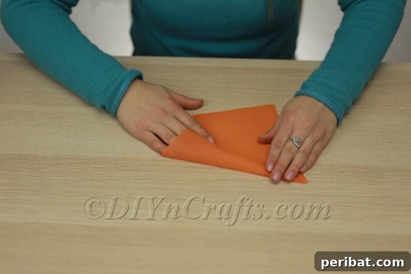 Orange fabric or paper being folded into a long, narrow cone shape, with edges being secured.