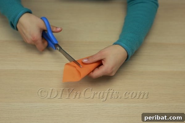 Scissors trimming the uneven top edge of the orange cone to create a straight opening.