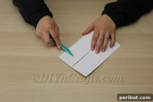Smoothing a clean fold on the paper template using a plastic knife for a sharp crease.