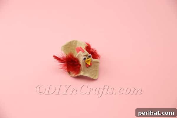 Red feathers being hot glued to the sides of the egg carton hen to create its wings.
