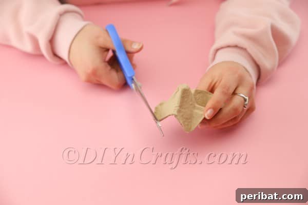 A close-up view of the egg carton being carefully cut with scissors to define the hen's shape.