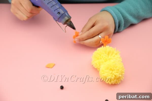 Craft Adorable Pom-Pom Easter Chicks at Home 18 Gluing the orange beak onto the chick's face