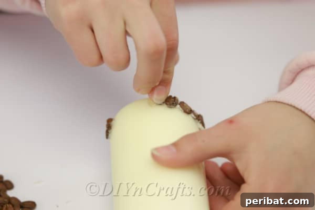Progress shot of placing coffee beans onto a pillar candle with hot glue, showing multiple rows of beans creating a decorative pattern.