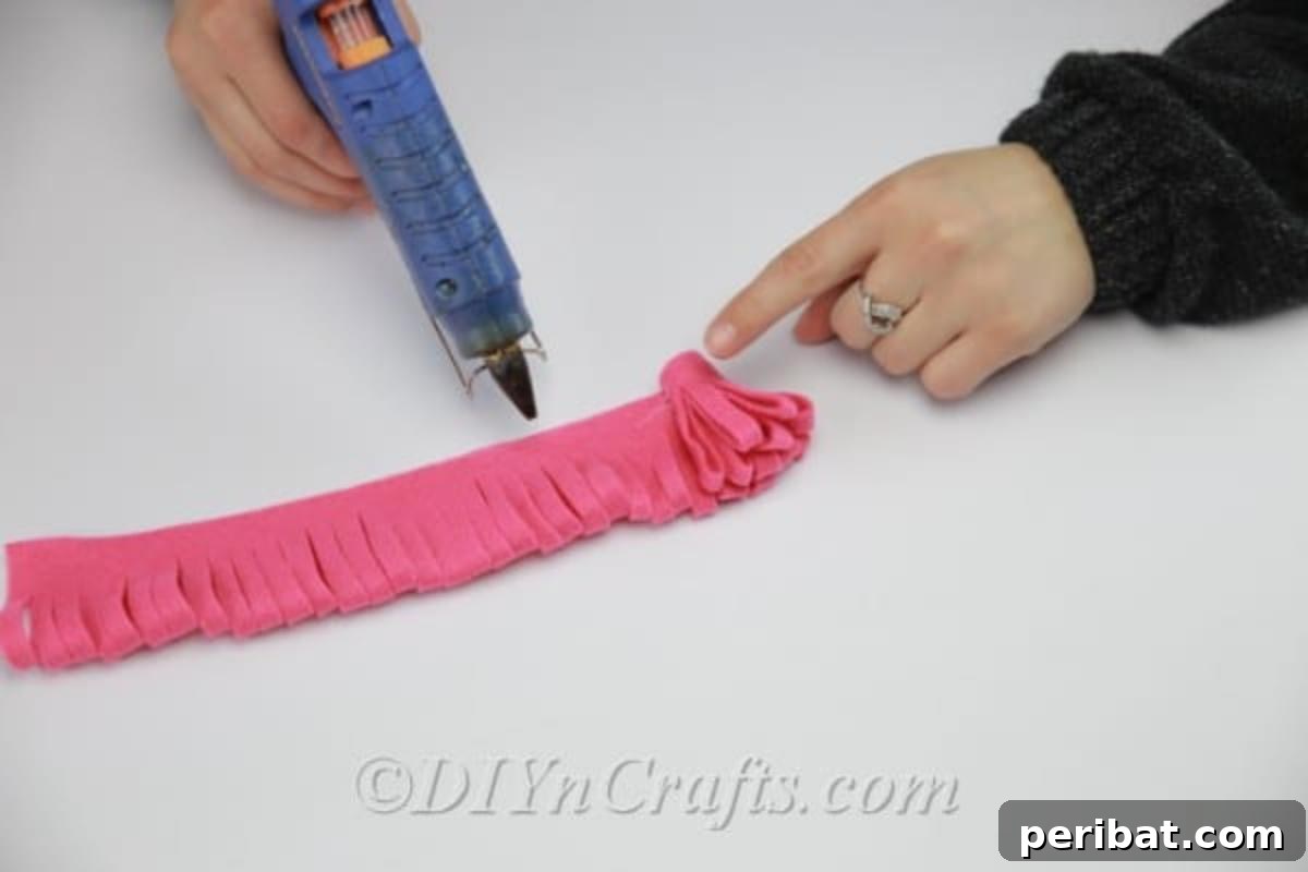 Rolling and gluing the fringed fabric strip to form the central part of the DIY fabric flower.