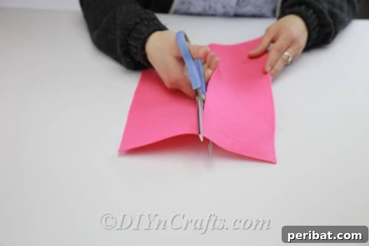 Cutting a piece of felt fabric in half lengthwise to prepare for making DIY flowers.