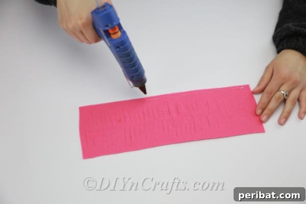Applying a line of hot glue to the center of the unfolded fringed fabric piece before refolding.