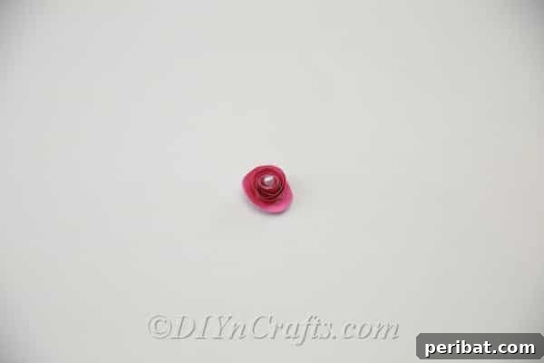 A close-up of a finished paper flower with a decorative pearl or bead glued firmly into its center.