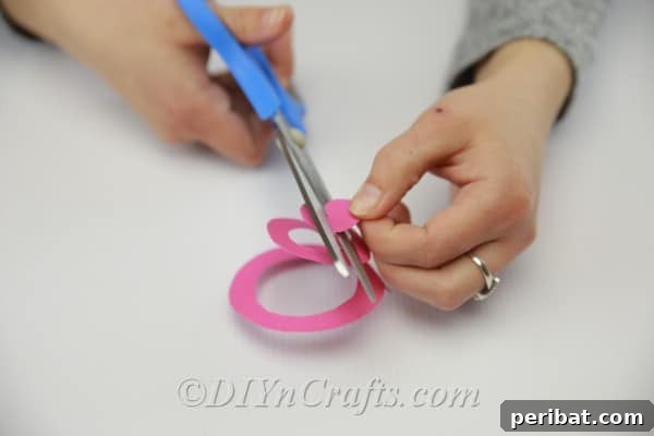 A hand carefully cutting a continuous swirl from the outer edge of a paper circle, creating a spiral strip.