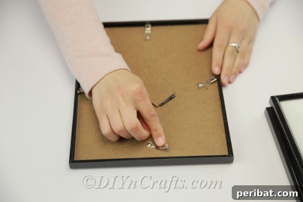 A hand is shown carefully removing the cardboard backing from a picture frame, revealing the glass pane.