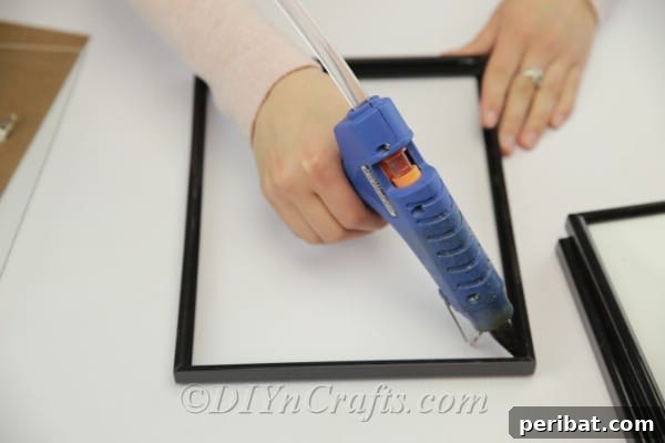 Close-up of a hand applying hot glue along the edge of a glass pane to secure it within a picture frame.