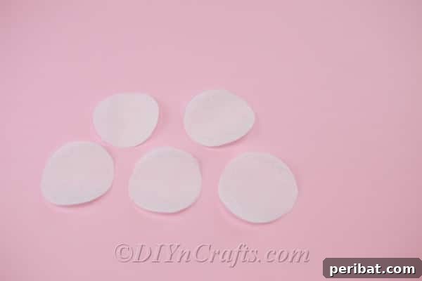 Applying a small dot of hot glue to the exact center of a fabric circle, preparing it for the initial fold to form a petal.