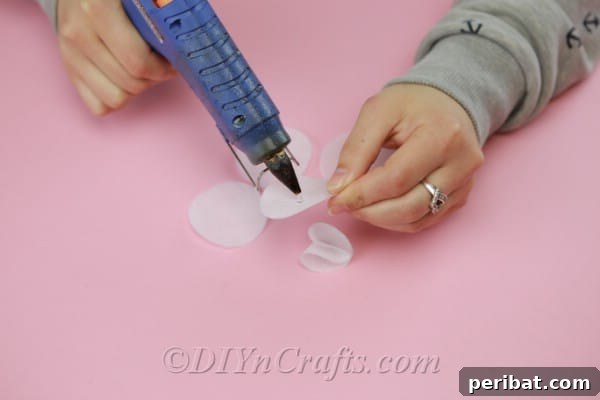 A fabric circle being folded in half over a dab of hot glue, forming the first stage of a dimensional flower petal.