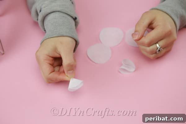 A completed, folded fabric petal being meticulously glued onto the base circle of a flower, positioned with the glued section towards the center.